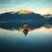 A serene, contemplative landscape depicting the essence of "Sein und Gewahrsein". In the foreground, a tranquil lake reflects the sky above, its mirrored surface a symbol of the objective reality. In the middle ground, a lone figure sits in meditative pose, their gaze inward, representing the subjective experience of consciousness. The background features a mountainous horizon, capped with snow and bathed in warm, golden light, conveying a sense of timeless, eternal being. The scene is captured with a wide, cinematic lens, emphasizing the depth and balance between the external world and the inner experience. The overall mood is one of stillness, harmony, and the profound interplay between existence and awareness.