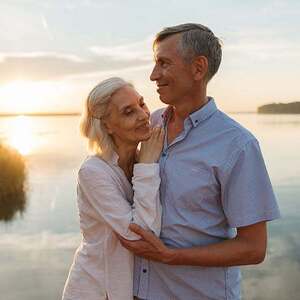 A senior couple lovingly embraces by a serene lake during a beautiful sunset.